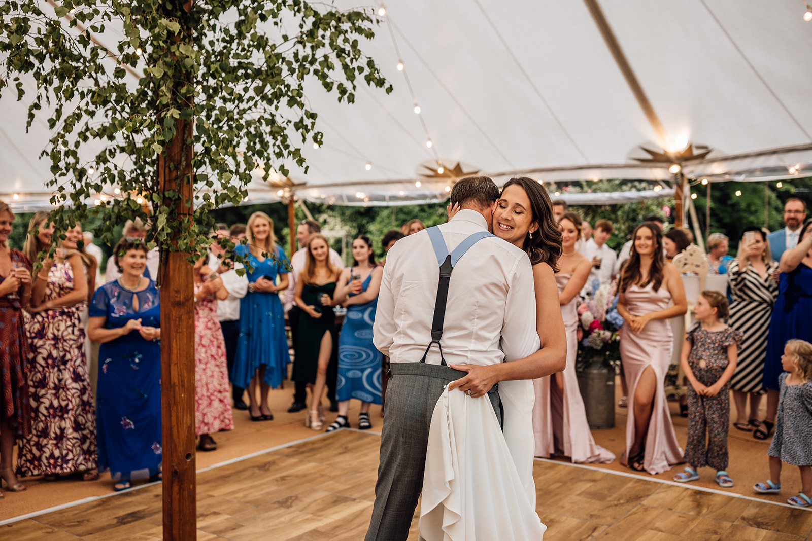 bride-and-groom-embrace-in-marquee-as-wedding-guests-watch